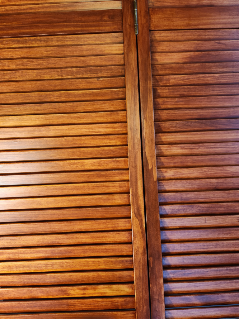A close-up of custom stained and sealed wooden slatted bifold doors.